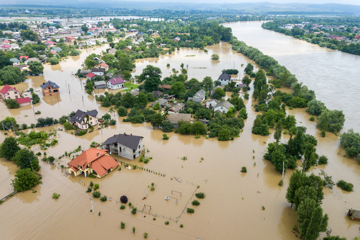 Aerial view of flooded residential area with submerged houses, trees, and streets, illustrating the impact of severe flooding.